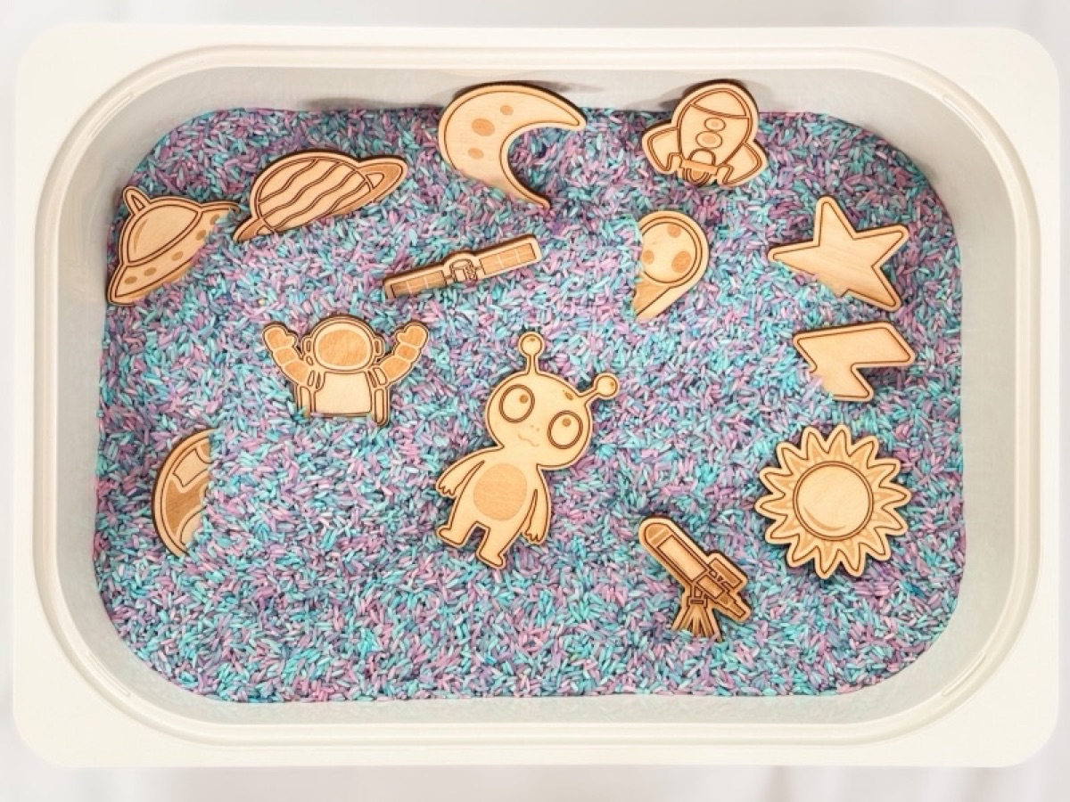 13-piece wooden space playscape set in a sensory bin of purple and blue rice