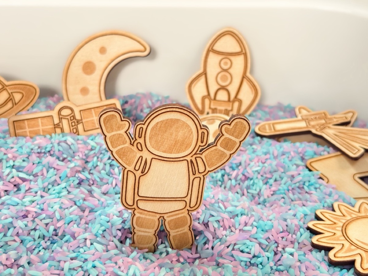 Laser-engraved Baltic birch astronaut standing in a sensory bin of colorful rice