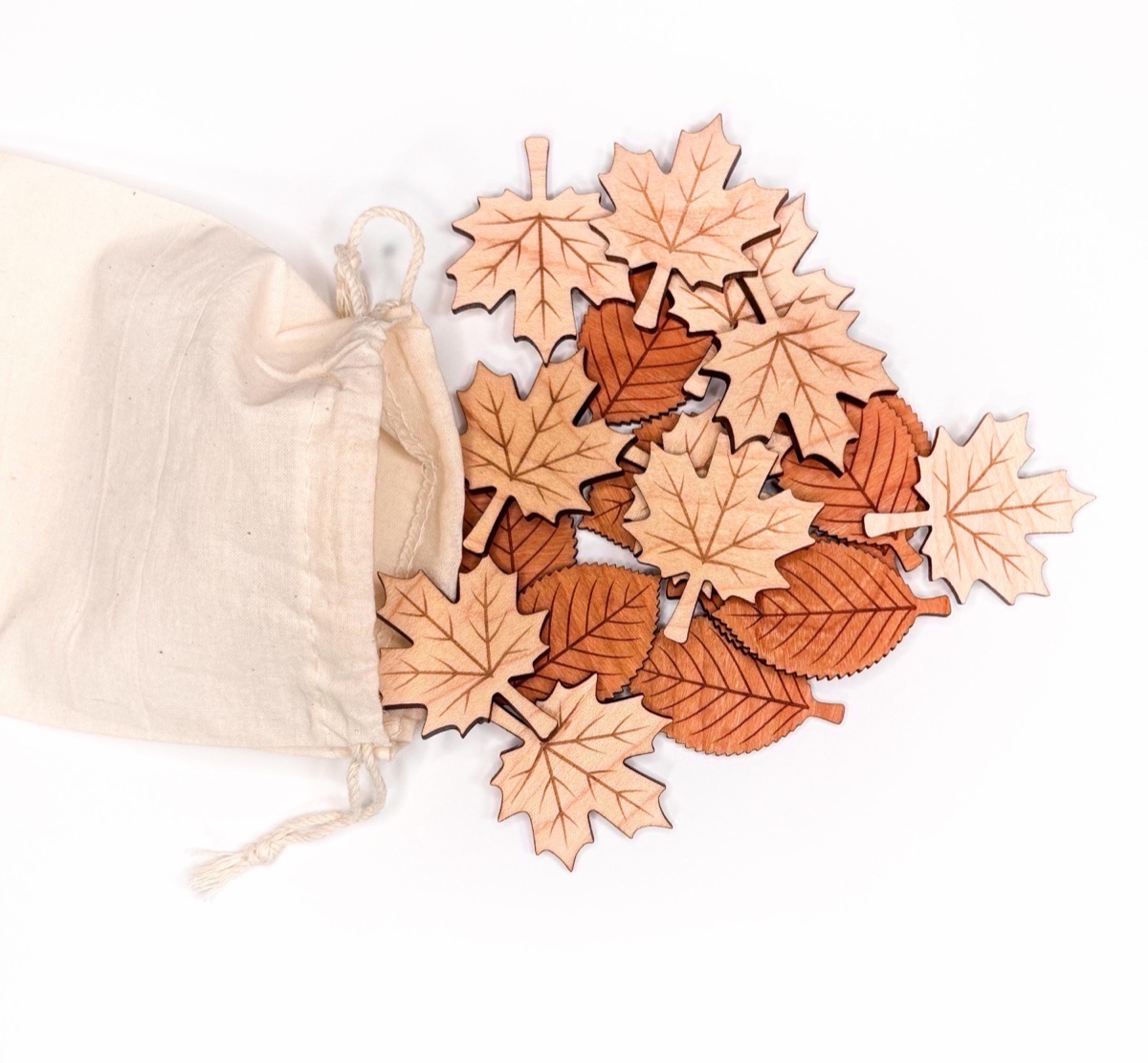 Wooden leaf counters in pale maple and warm cherry spilling from a cotton drawstring bag